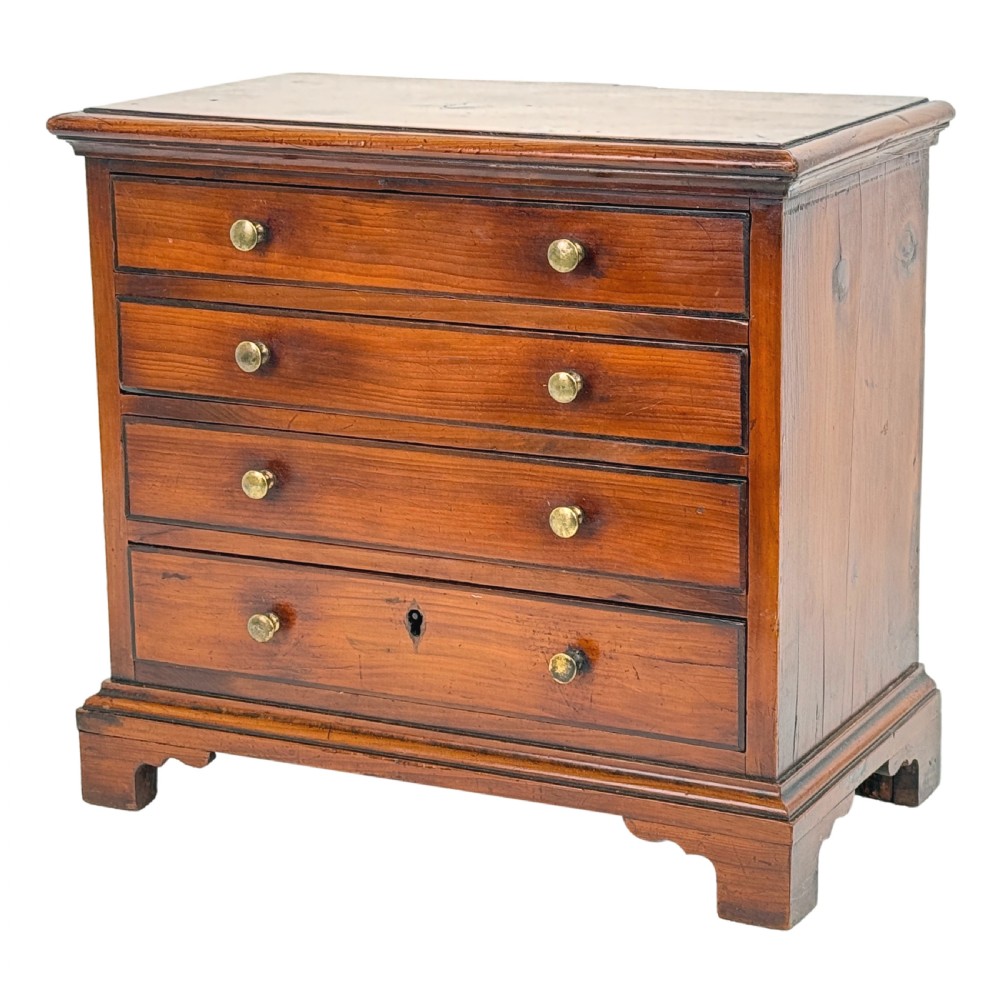 A Georgian miniature yew wood chest of four drawers featuring brass knobs, a keyhole escutcheon, and bracket feet.