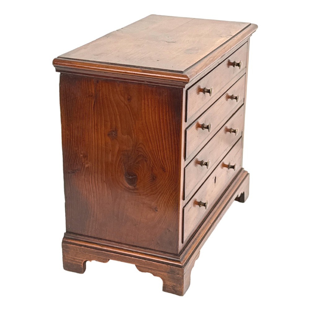 A Georgian miniature yew wood chest of four drawers featuring brass knobs, a keyhole escutcheon, and bracket feet. View III