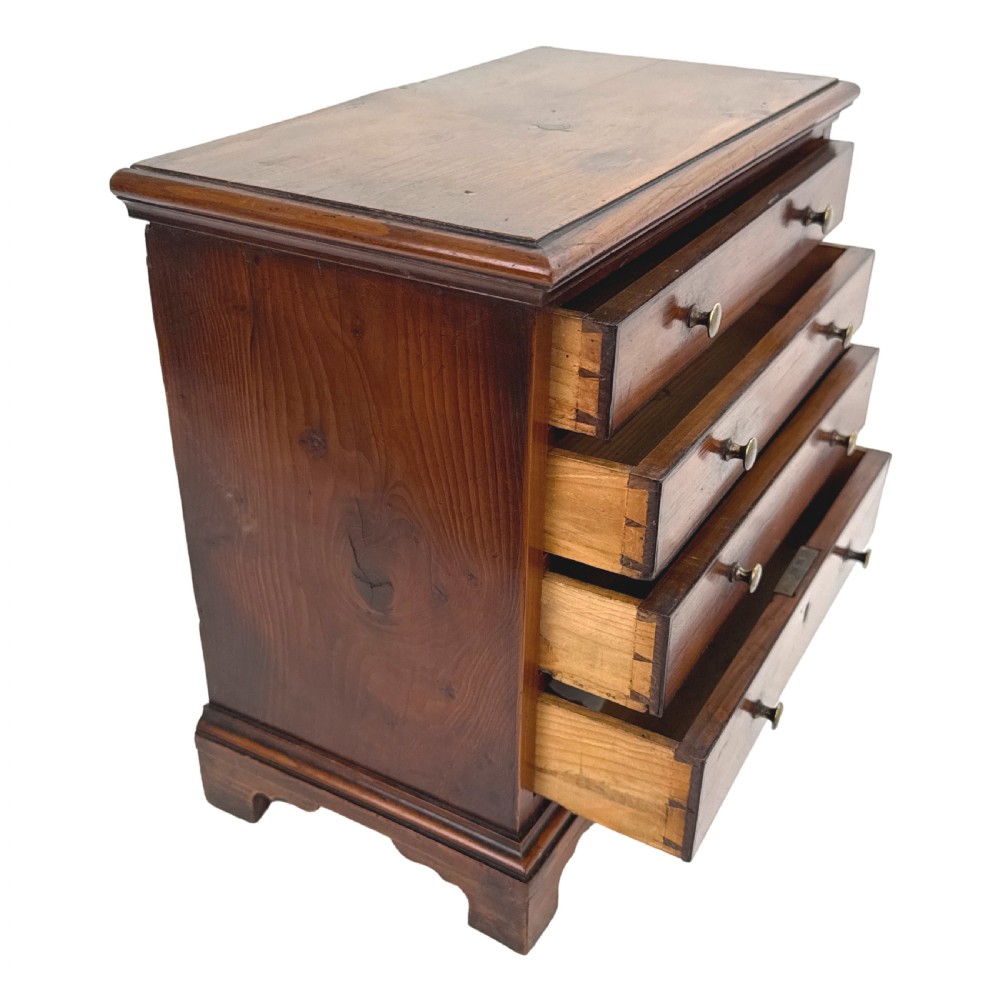 A Georgian miniature yew wood chest of four drawers featuring brass knobs, a keyhole escutcheon, and bracket feet. View IV