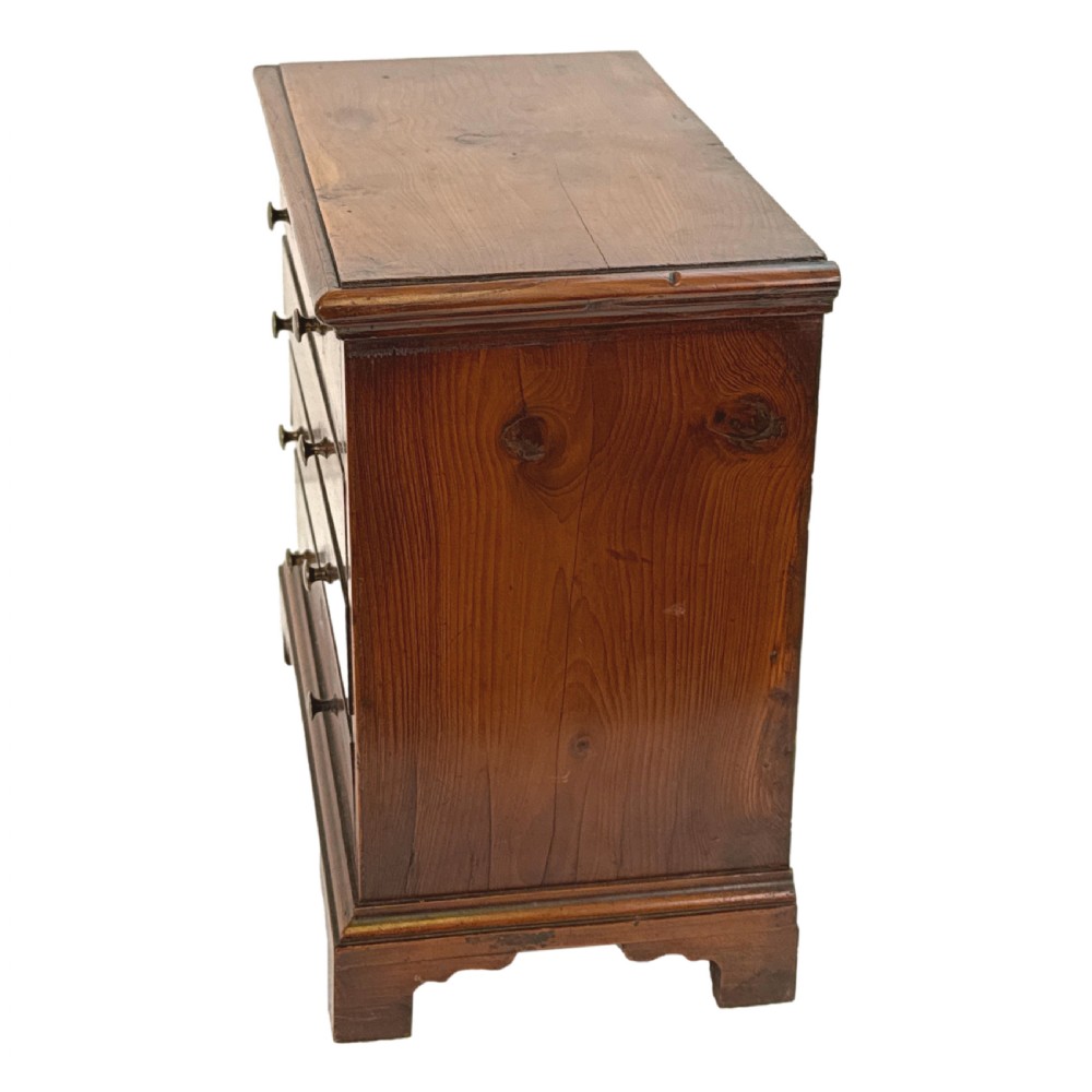 A Georgian miniature yew wood chest of four drawers featuring brass knobs, a keyhole escutcheon, and bracket feet. View V