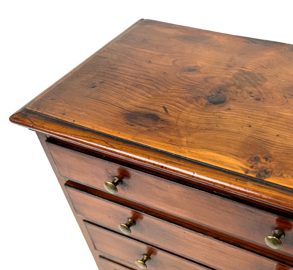 A Georgian miniature yew wood chest of four drawers featuring brass knobs, a keyhole escutcheon, and bracket feet. View VI