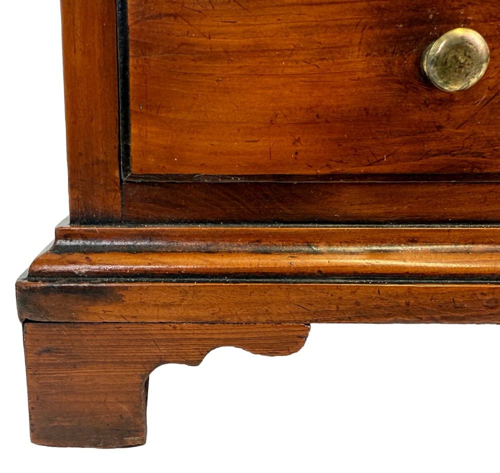 A Georgian miniature yew wood chest of four drawers featuring brass knobs, a keyhole escutcheon, and bracket feet. View VIII