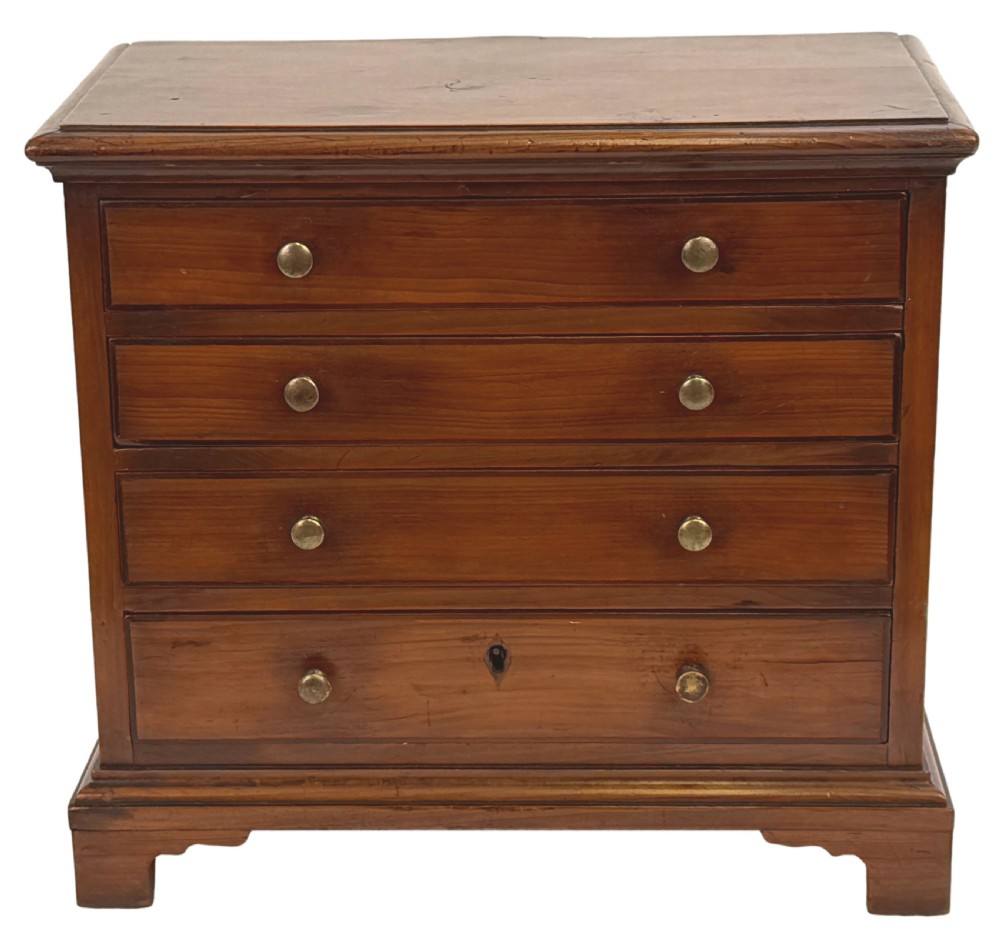 A Georgian miniature yew wood chest of four drawers featuring brass knobs, a keyhole escutcheon, and bracket feet. View X