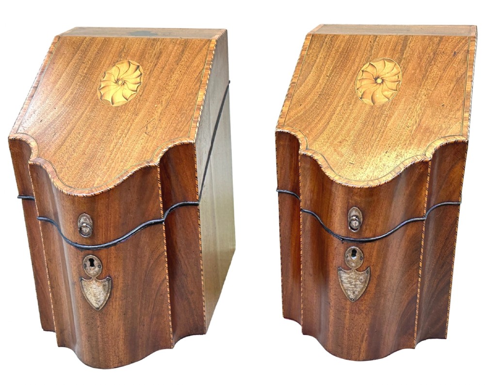 A pair of Georgian mahogany knife boxes featuring sloping lids with inlaid shell motifs, serpentine fronts, and metal keyhole escutcheons.