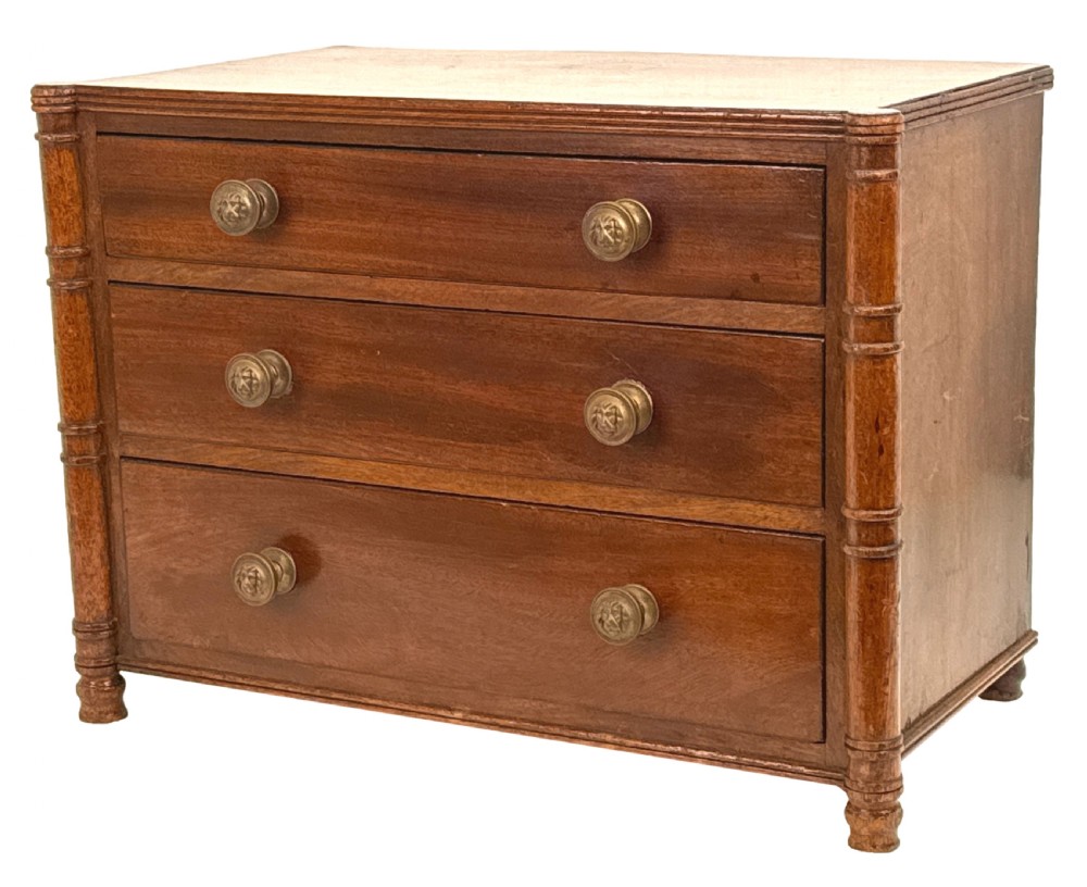 A Regency period miniature mahogany chest featuring three graduated drawers with round knobs and reeded corner columns.