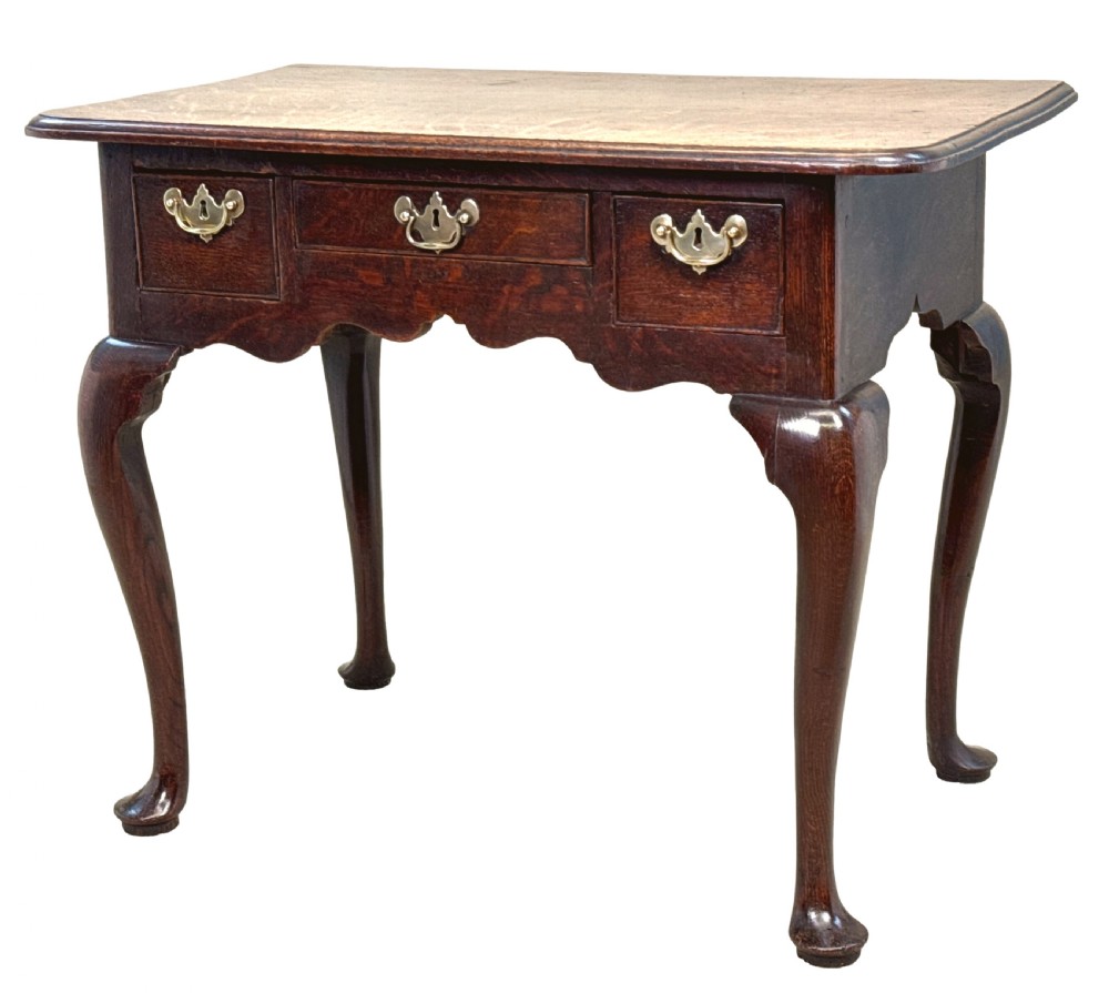 An 18th-century Georgian oak lowboy featuring three drawers with brass handles, a shaped apron, and four cabriole legs with pad feet.