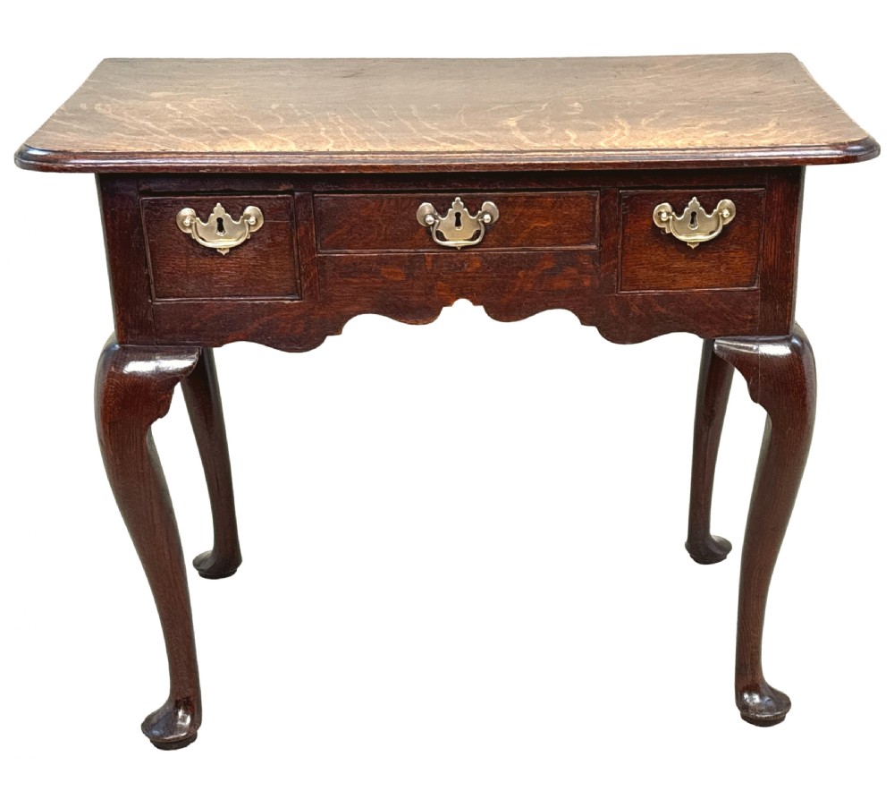 An 18th-century Georgian oak lowboy featuring three drawers with brass handles, a shaped apron, and four cabriole legs with pad feet. View X