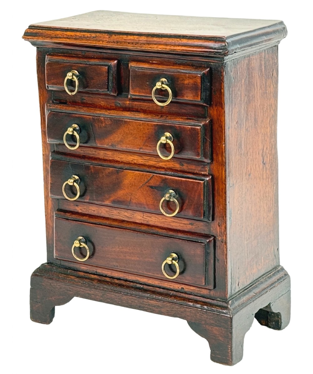 A miniature 18th-century mahogany chest of drawers featuring two small drawers over three long drawers with brass ring drop handles and bracket feet.