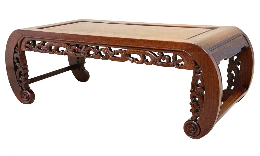 A low dark hardwood coffee table featuring an openwork carved apron and inward-curving scroll legs.
