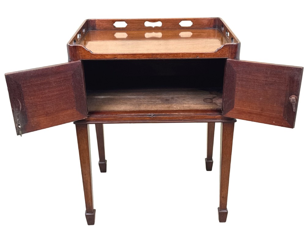 An 18th-century Georgian mahogany bedside table featuring a pierced tray top gallery with cut-out handles, double cupboard doors with a central brass pull, and square tapered legs. View VII