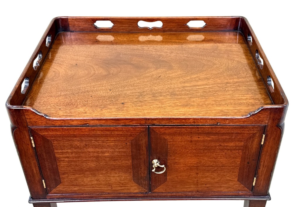 An 18th-century Georgian mahogany bedside table featuring a pierced tray top gallery with cut-out handles, double cupboard doors with a central brass pull, and square tapered legs. View IX