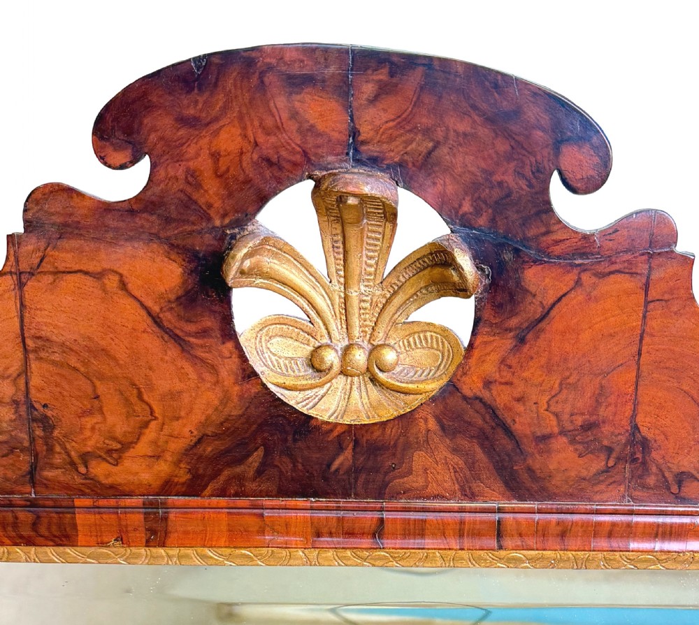 An 18th-century George II wall mirror featuring a figured walnut frame with a carved giltwood inner border, side drapery tassels, and a central carved plume cresting. View II