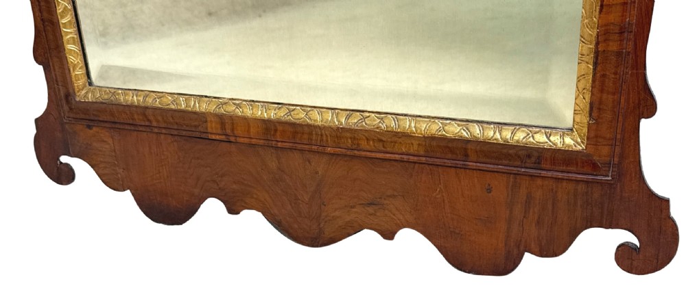 An 18th-century George II wall mirror featuring a figured walnut frame with a carved giltwood inner border, side drapery tassels, and a central carved plume cresting. View VII