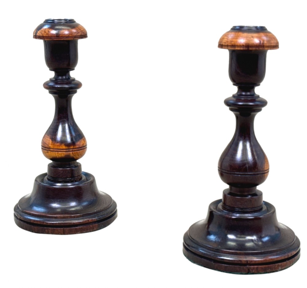 A pair of 19th-century turned lignum vitae wooden candlesticks featuring baluster-form stems, stepped circular bases, and contrasting dark and light graining.
