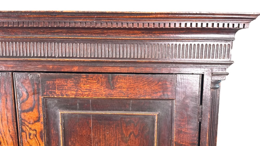 An 18th-century Georgian dark oak press cupboard featuring an upper double-door cabinet with fielded panels over a chest of drawers with brass handles. View X