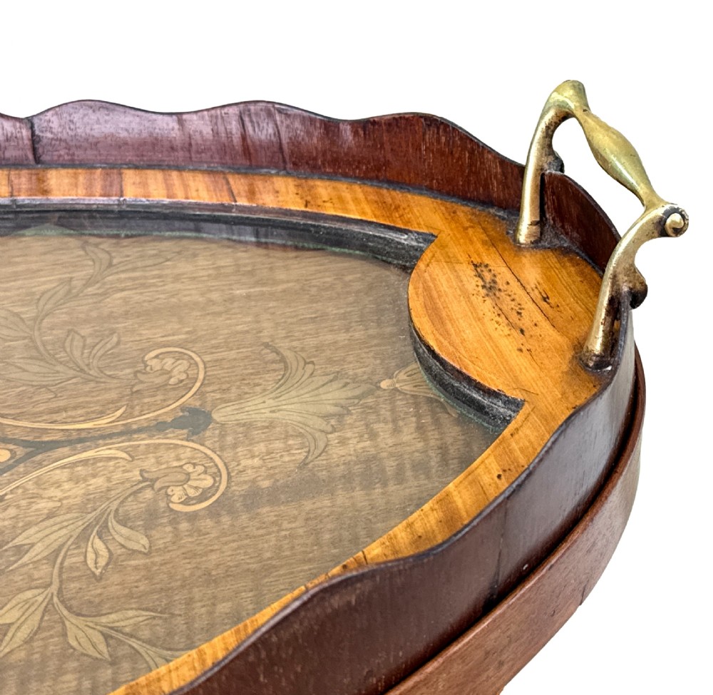 A 19th-century oval two-tier mahogany table featuring satinwood marquetry inlay, a scalloped top tier gallery with brass handles, and curved legs. View X