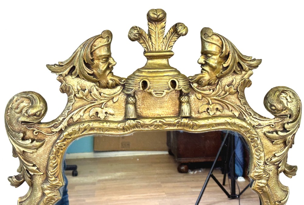 A tall late nineteenth-century carved giltwood wall mirror featuring elaborate cresting with carved sculpted heads, foliage motifs, and scrollwork. View IV