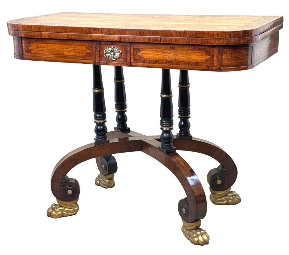 A nineteenth-century Regency kingwood card table with an inlaid fold-over top, ebonised turned pillar supports, and splayed legs with gilded lion paw feet.