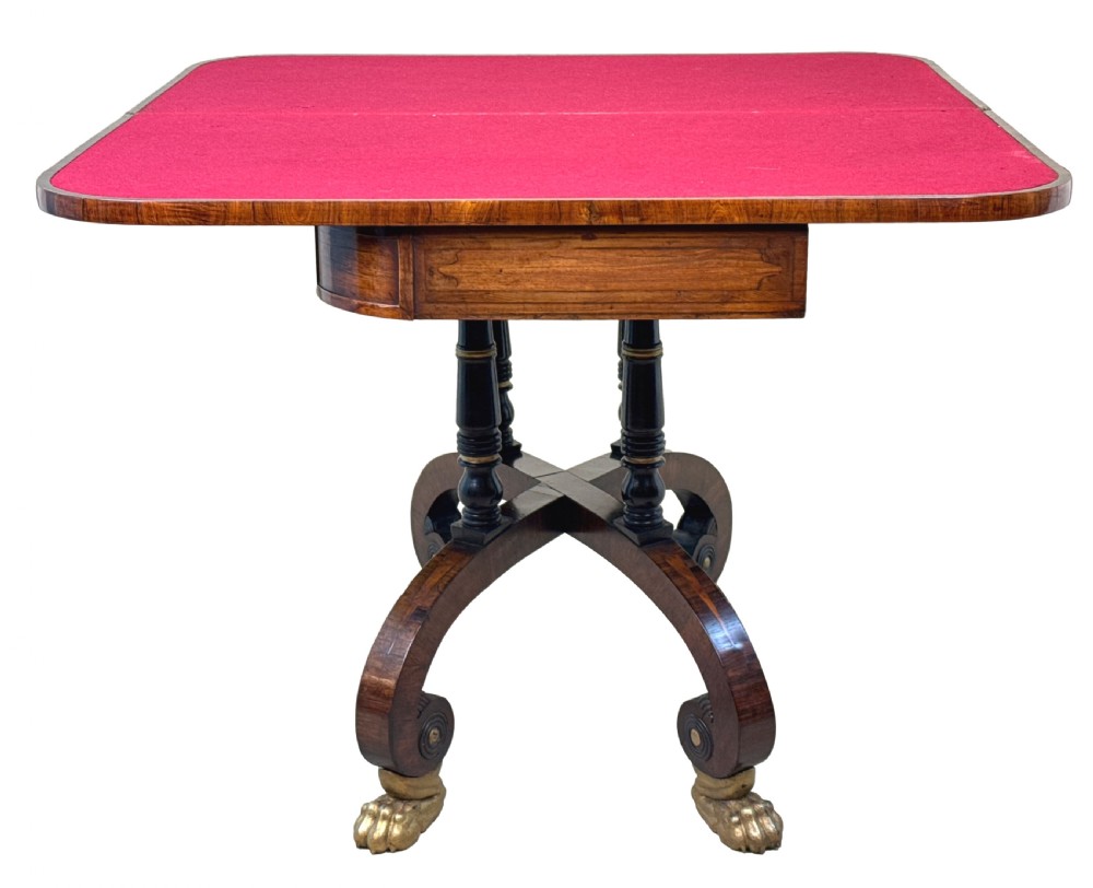 A nineteenth-century Regency kingwood card table with an inlaid fold-over top, ebonised turned pillar supports, and splayed legs with gilded lion paw feet. View IV