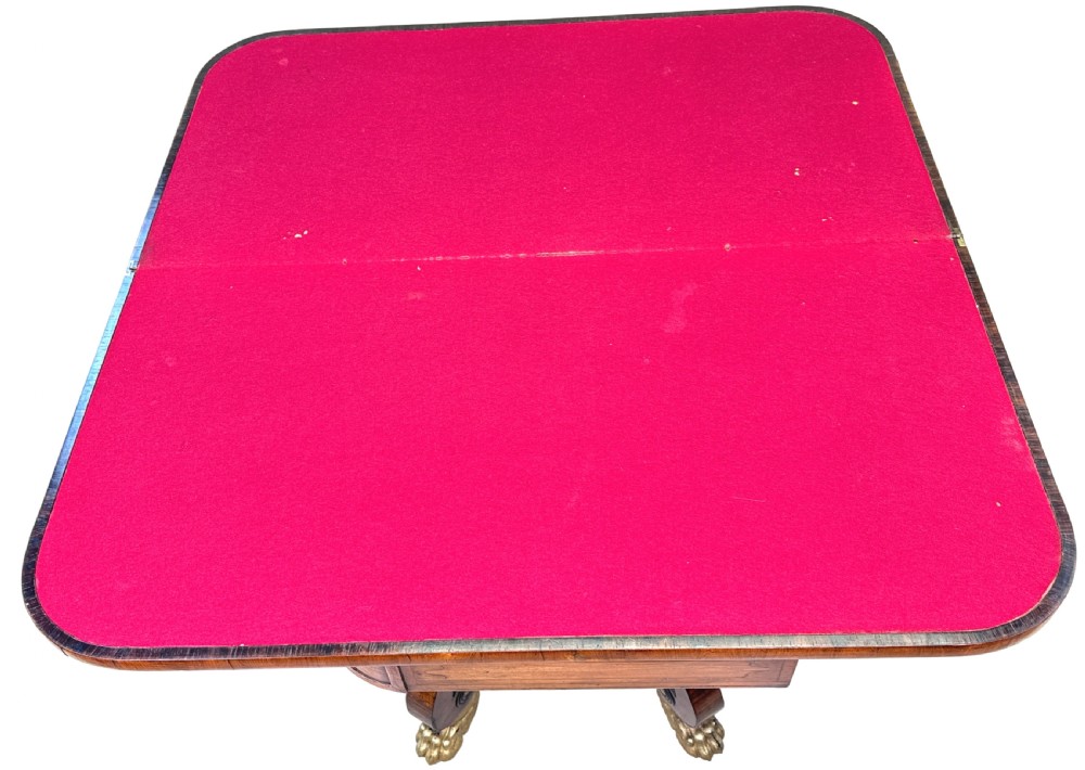 A nineteenth-century Regency kingwood card table with an inlaid fold-over top, ebonised turned pillar supports, and splayed legs with gilded lion paw feet. View VI