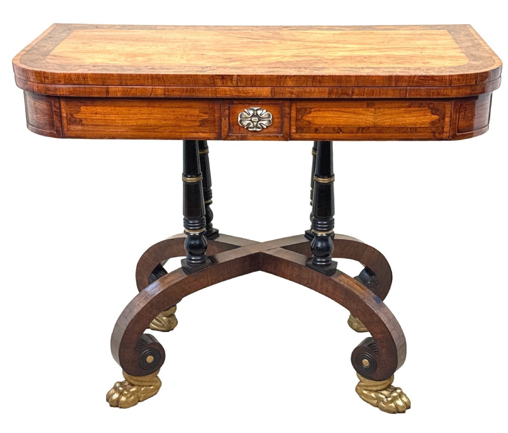 A nineteenth-century Regency kingwood card table with an inlaid fold-over top, ebonised turned pillar supports, and splayed legs with gilded lion paw feet. View XV