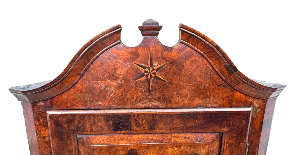 An antique Queen Anne burr walnut wall-hanging corner cupboard featuring an arched pediment with an inlaid star motif and a single fielded panel door. View II