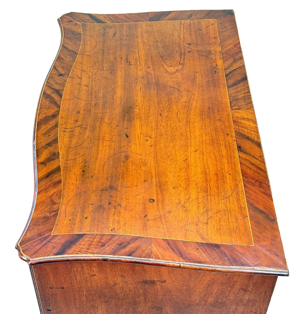 A George III mahogany serpentine chest of drawers featuring four graduated drawers with brass handles and inlaid stringing, supported on bracket feet. View II