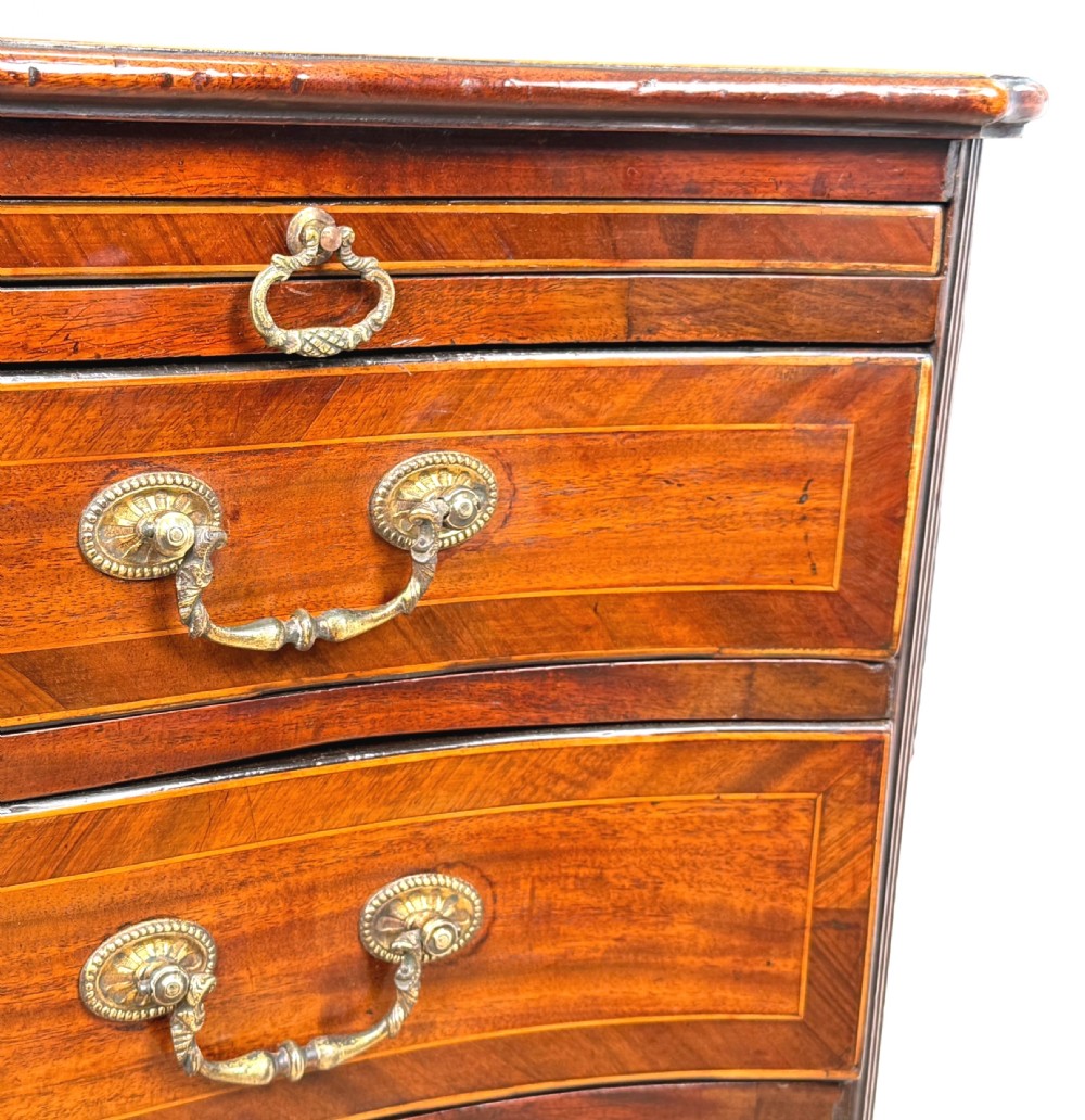 A George III mahogany serpentine chest of drawers featuring four graduated drawers with brass handles and inlaid stringing, supported on bracket feet. View X