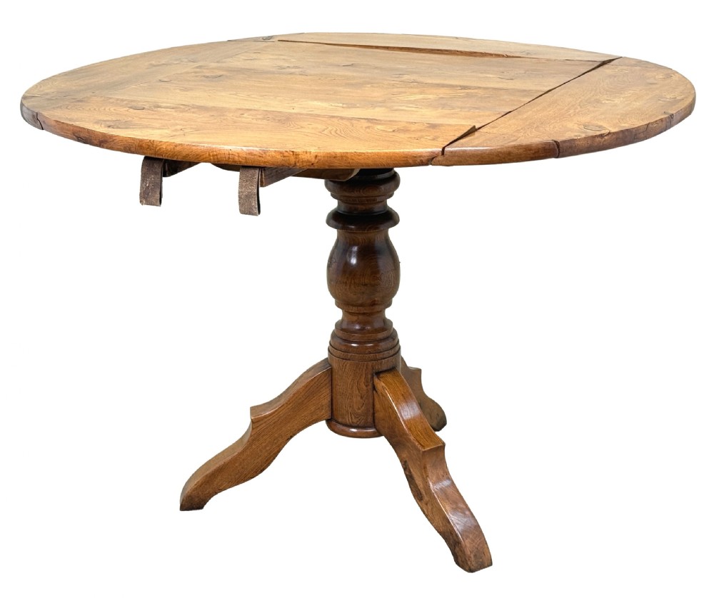A nineteenth-century French Provincial elm centre table featuring a round top with two drop leaves, a turned central pedestal, and a three-legged tripod base.