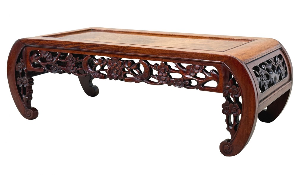 A low-profile 19th-century Oriental hardwood coffee table featuring an intricately carved floral apron and inwardly curved scroll legs.