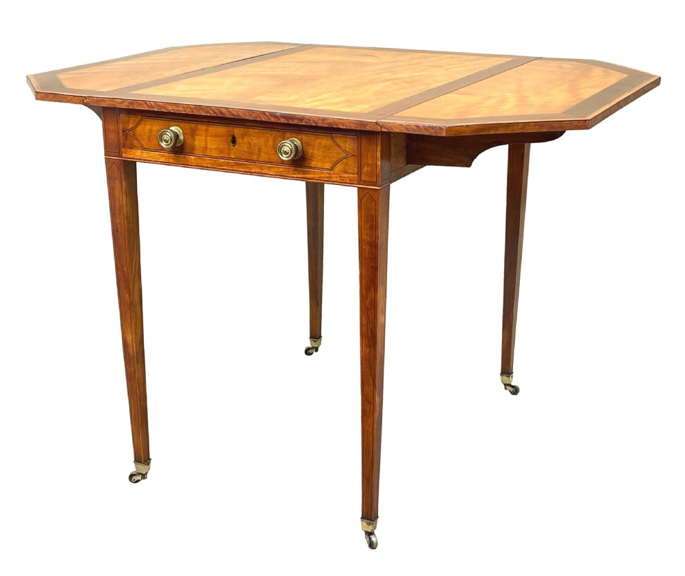 A late 18th-century Georgian satinwood Pembroke table featuring two hinged drop leaves, dark wood crossbanding, a drawer with brass knobs, and tapered square legs with castors.