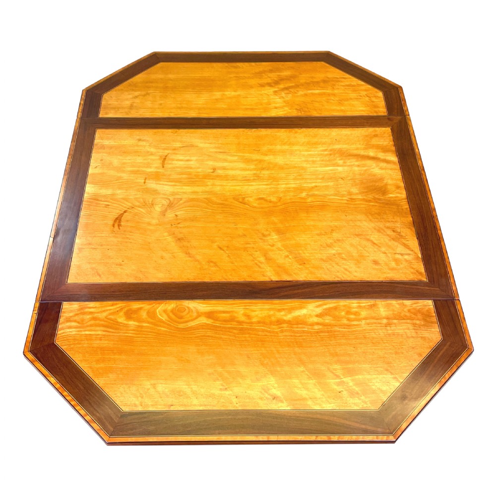 A late 18th-century Georgian satinwood Pembroke table featuring two hinged drop leaves, dark wood crossbanding, a drawer with brass knobs, and tapered square legs with castors. View II