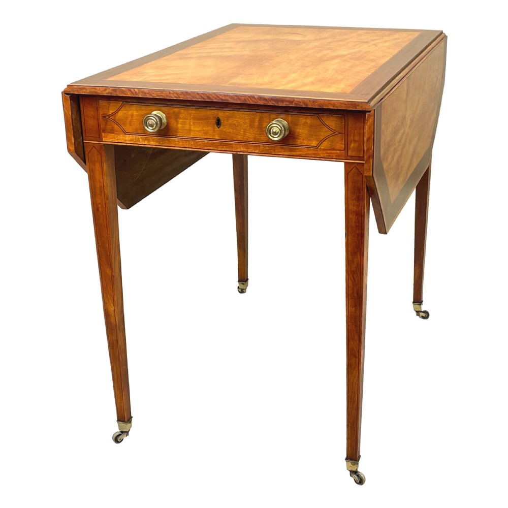 A late 18th-century Georgian satinwood Pembroke table featuring two hinged drop leaves, dark wood crossbanding, a drawer with brass knobs, and tapered square legs with castors. View III