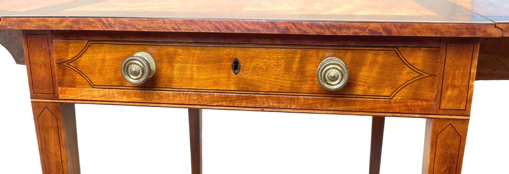 A late 18th-century Georgian satinwood Pembroke table featuring two hinged drop leaves, dark wood crossbanding, a drawer with brass knobs, and tapered square legs with castors. View IV