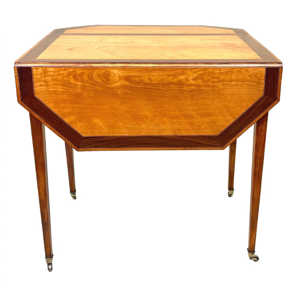 A late 18th-century Georgian satinwood Pembroke table featuring two hinged drop leaves, dark wood crossbanding, a drawer with brass knobs, and tapered square legs with castors. View V