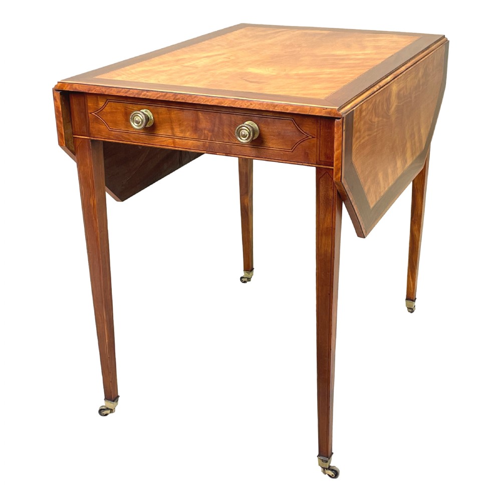 A late 18th-century Georgian satinwood Pembroke table featuring two hinged drop leaves, dark wood crossbanding, a drawer with brass knobs, and tapered square legs with castors. View VI
