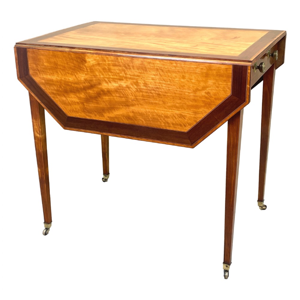 A late 18th-century Georgian satinwood Pembroke table featuring two hinged drop leaves, dark wood crossbanding, a drawer with brass knobs, and tapered square legs with castors. View XI