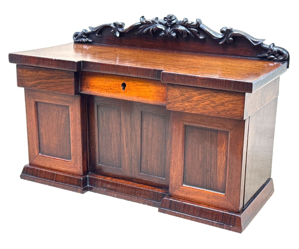A dark rosewood tea caddy crafted in the shape of a miniature Regency breakfront sideboard with a carved cresting backboard.