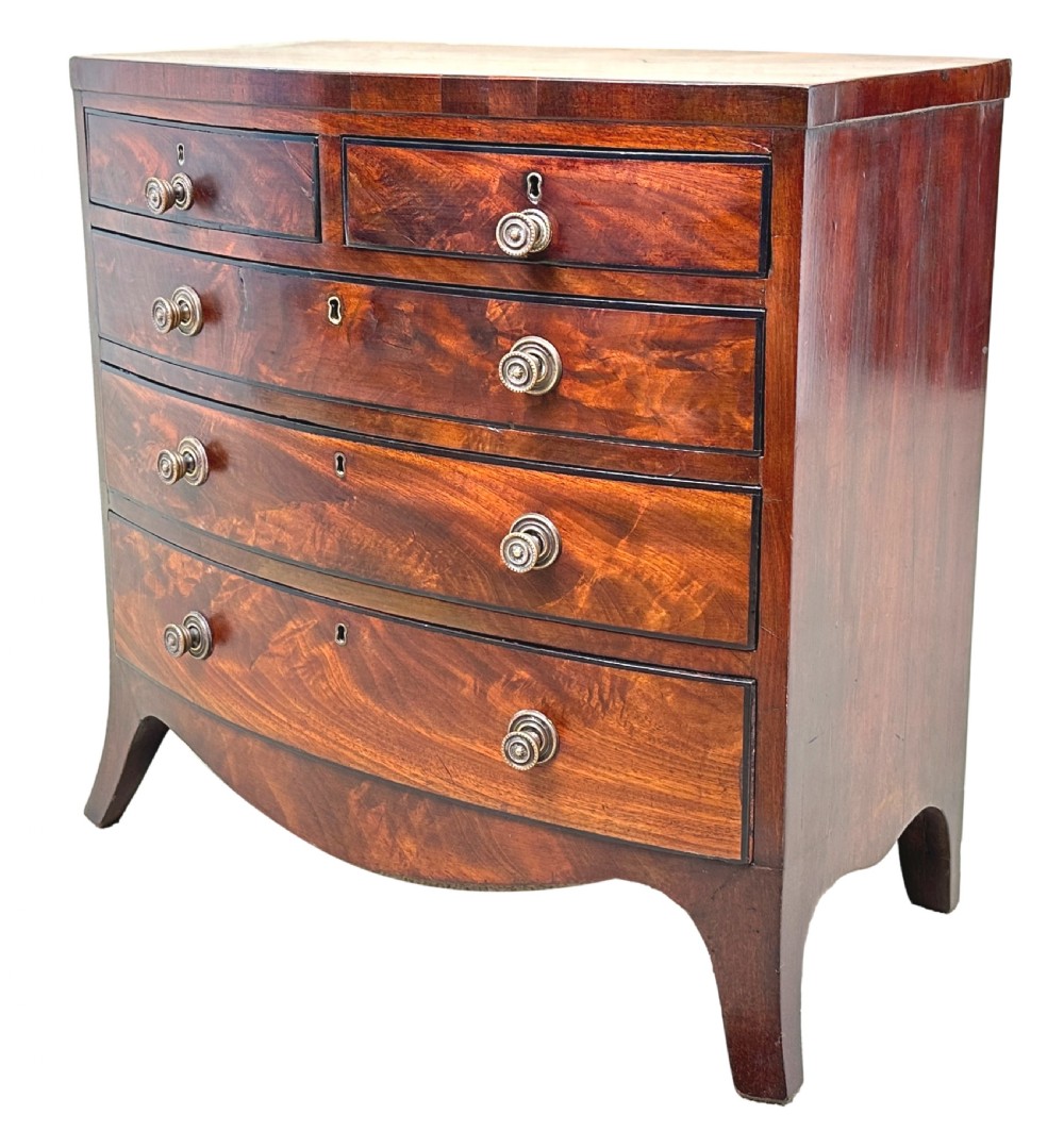 A Georgian mahogany miniature bowfront chest of drawers with flame mahogany drawer fronts, turned brass handles, and splayed bracket feet.