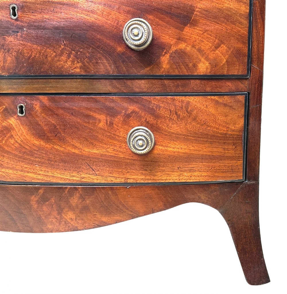 A Georgian mahogany miniature bowfront chest of drawers with flame mahogany drawer fronts, turned brass handles, and splayed bracket feet. View VI