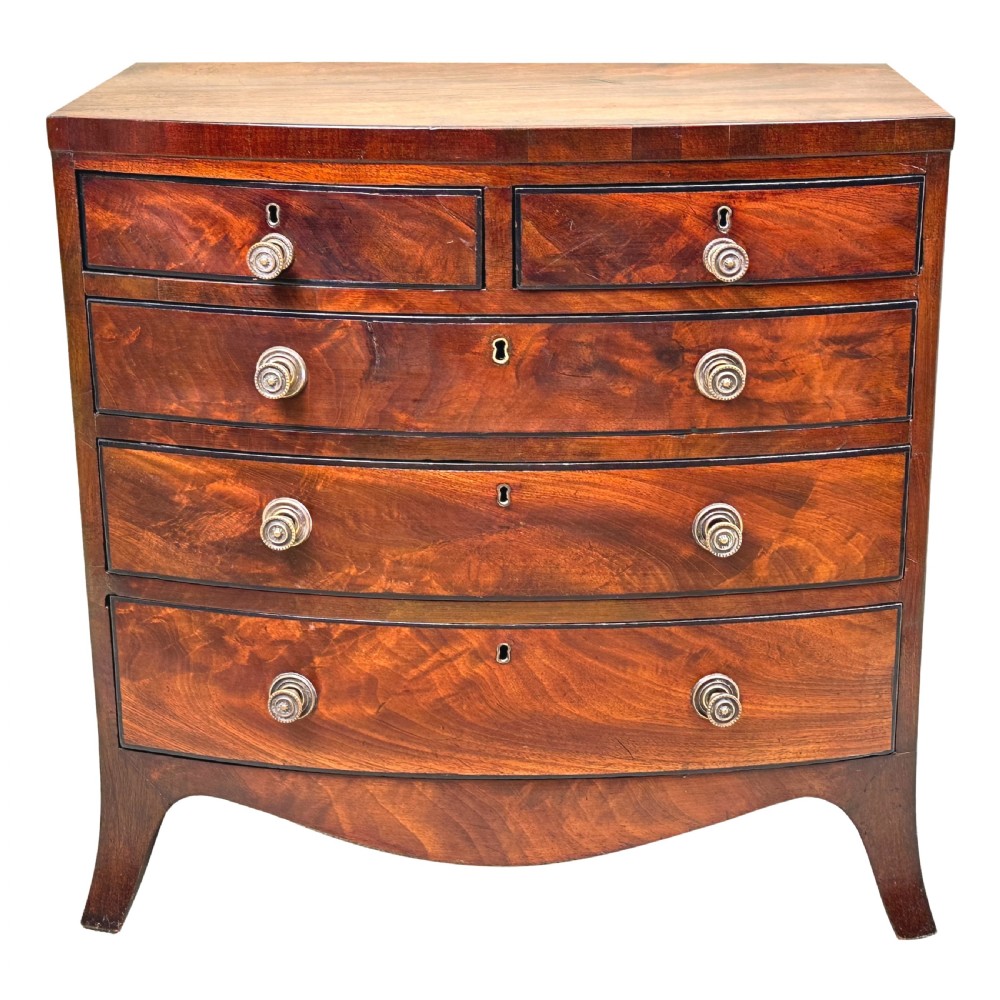 A Georgian mahogany miniature bowfront chest of drawers with flame mahogany drawer fronts, turned brass handles, and splayed bracket feet. View IX