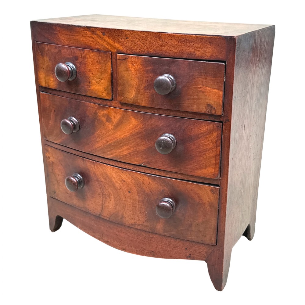 A Victorian miniature mahogany bowfront chest featuring two short over two long drawers with turned wooden knobs and bracket feet.