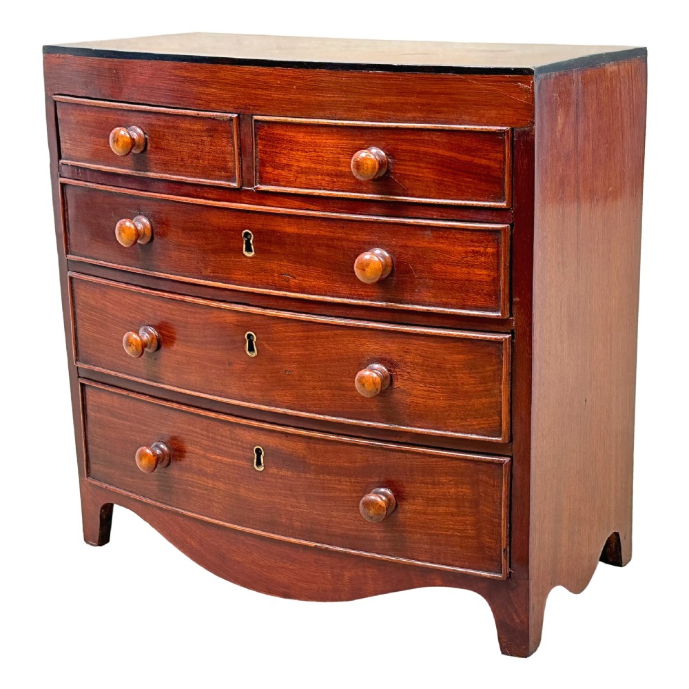 A Regency miniature mahogany bowfront chest featuring two short over three long graduated drawers with turned wooden knobs and brass keyhole escutcheons. View III