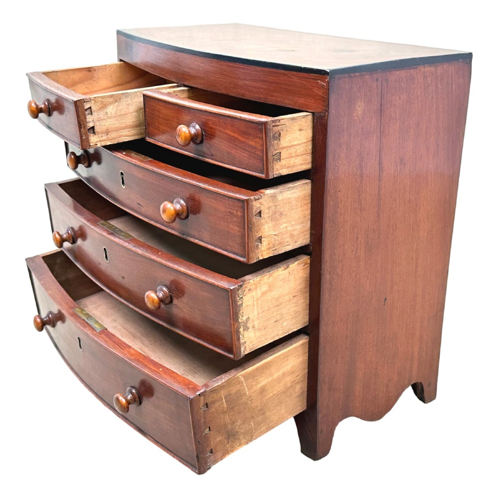 A Regency miniature mahogany bowfront chest featuring two short over three long graduated drawers with turned wooden knobs and brass keyhole escutcheons. View V
