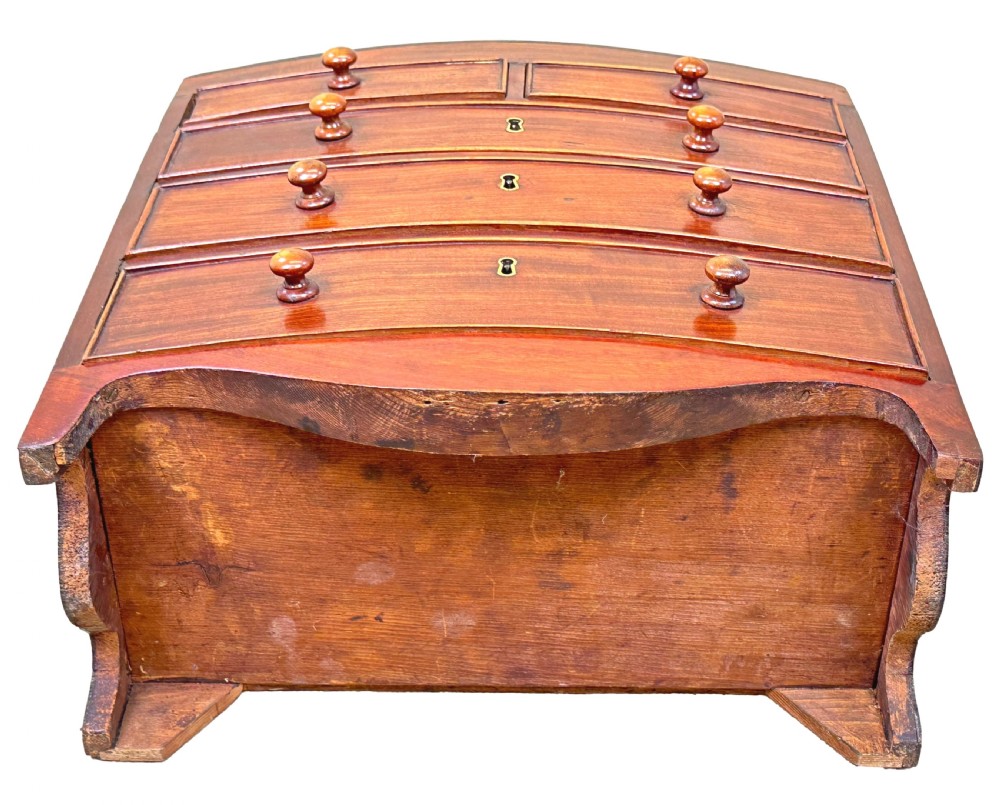 A Regency miniature mahogany bowfront chest featuring two short over three long graduated drawers with turned wooden knobs and brass keyhole escutcheons. View VI