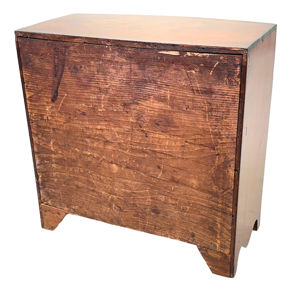 A Regency miniature mahogany bowfront chest featuring two short over three long graduated drawers with turned wooden knobs and brass keyhole escutcheons. View VII