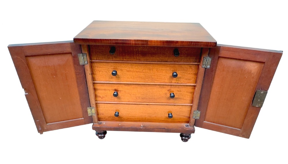 A Regency flame mahogany twin-door miniature table cabinet with turned feet, bead moulding, and brass escutcheons. View IV