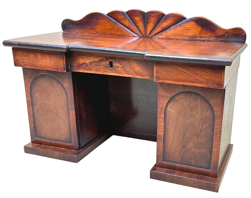A miniature Regency mahogany tea caddy crafted in the form of a pedestal sideboard with a fan-carved cresting backrail.