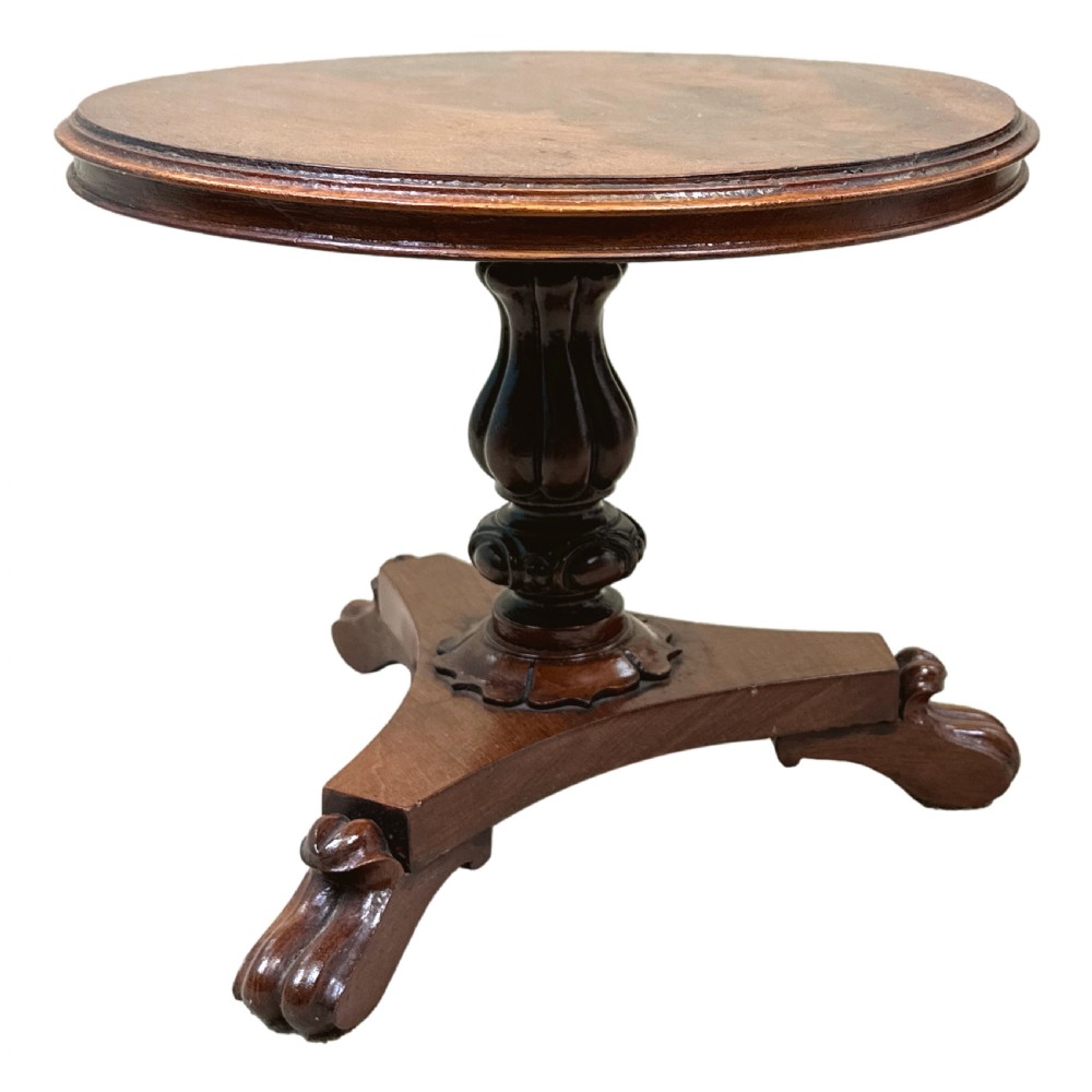 A mid-19th-century miniature circular mahogany centre table featuring a turned central column and a triform base with carved feet.