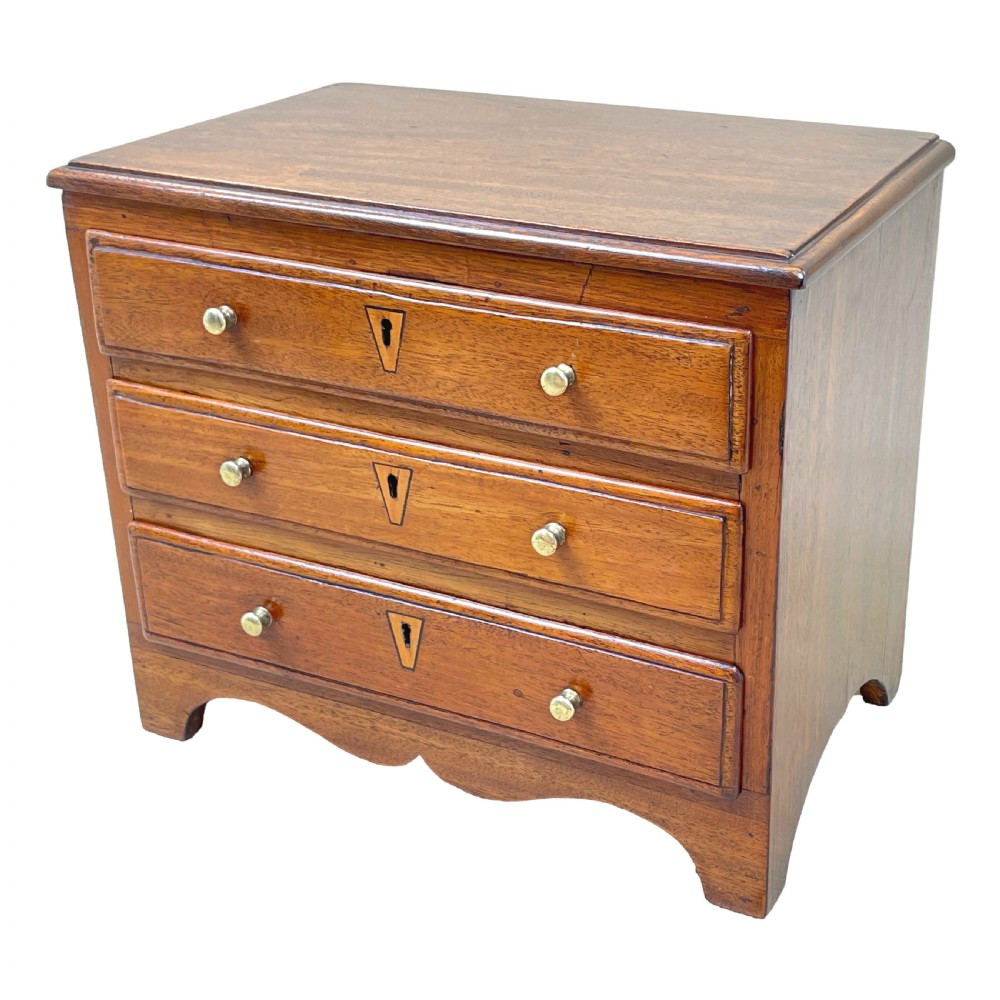 A small Georgian mahogany miniature chest featuring three drawers with brass knob handles, diamond-shaped escutcheons, and a shaped apron.